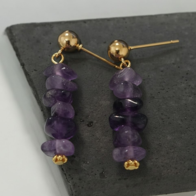 Gros plan sur les boucles d'oreilles en améthyste avec clous massifs dorés, mettant en avant la qualité de la monture.