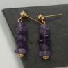 Gros plan sur les boucles d'oreilles en améthyste avec clous massifs dorés, mettant en avant la qualité de la monture.