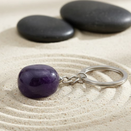 Porte-clé galet d'améthyste naturelle sur un fond zen de sable et galets noirs.